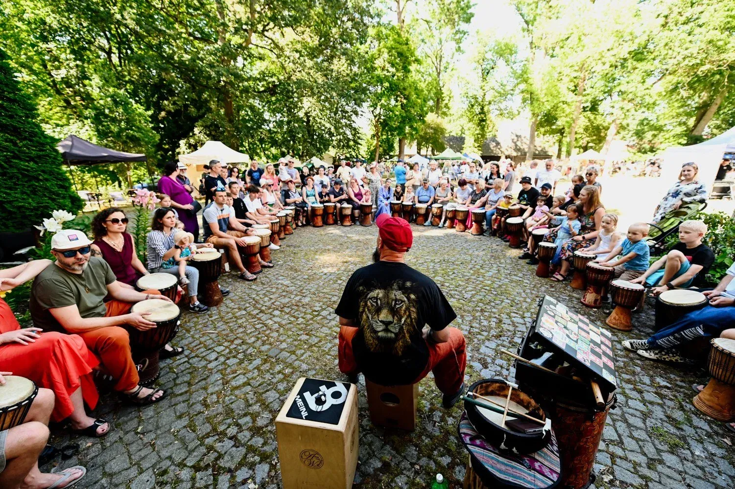 Warsztat bębniarski: duże koło dorosłych i dzieci z bębnami djembe na zamkowym dziedzińcu