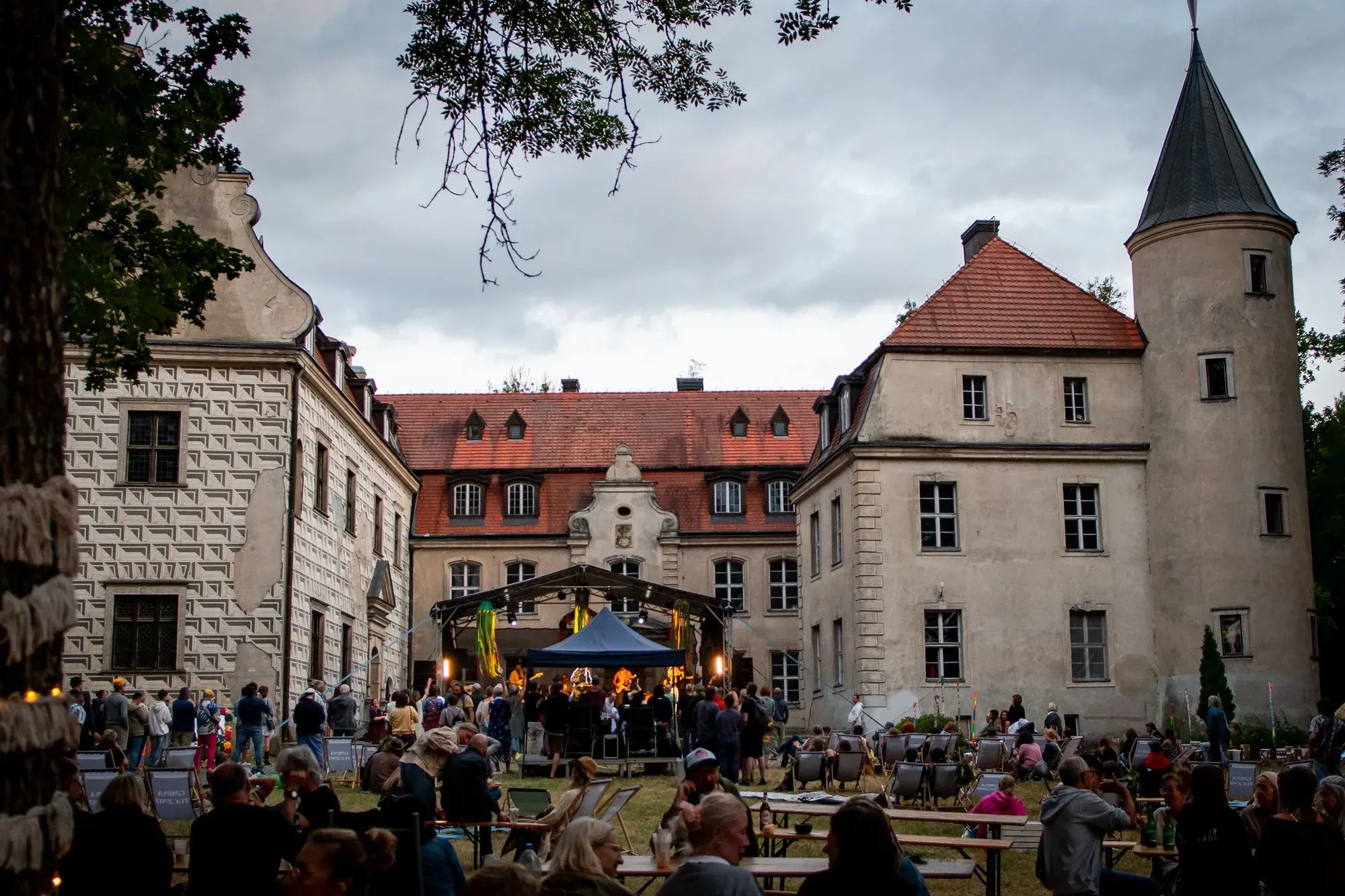 Dziedziniec Zamku Tuczno wieczorem, ze sceną z koncertem i publicznością siedzącą na trawie